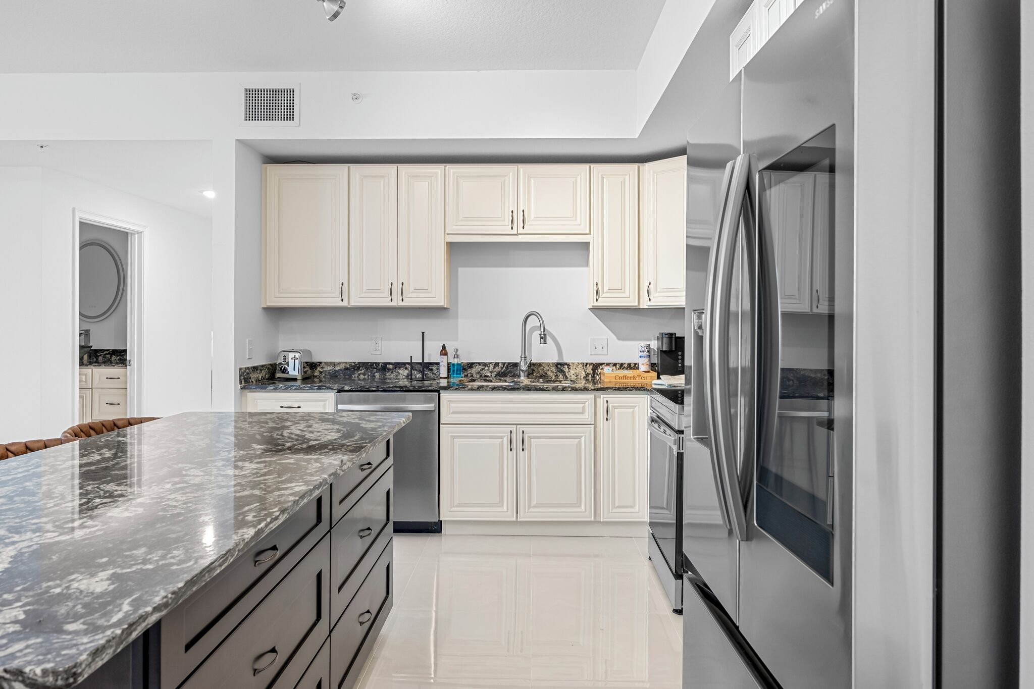 A modern kitchen with white cabinets, a marble countertop, stainless steel appliances, and a built-in oven.
