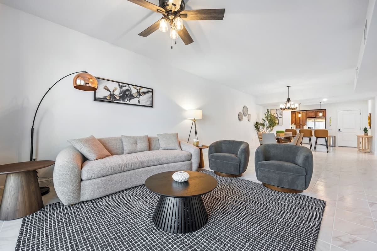 A modern living room with a sofa, two armchairs, a coffee table, and a dining area in the background.