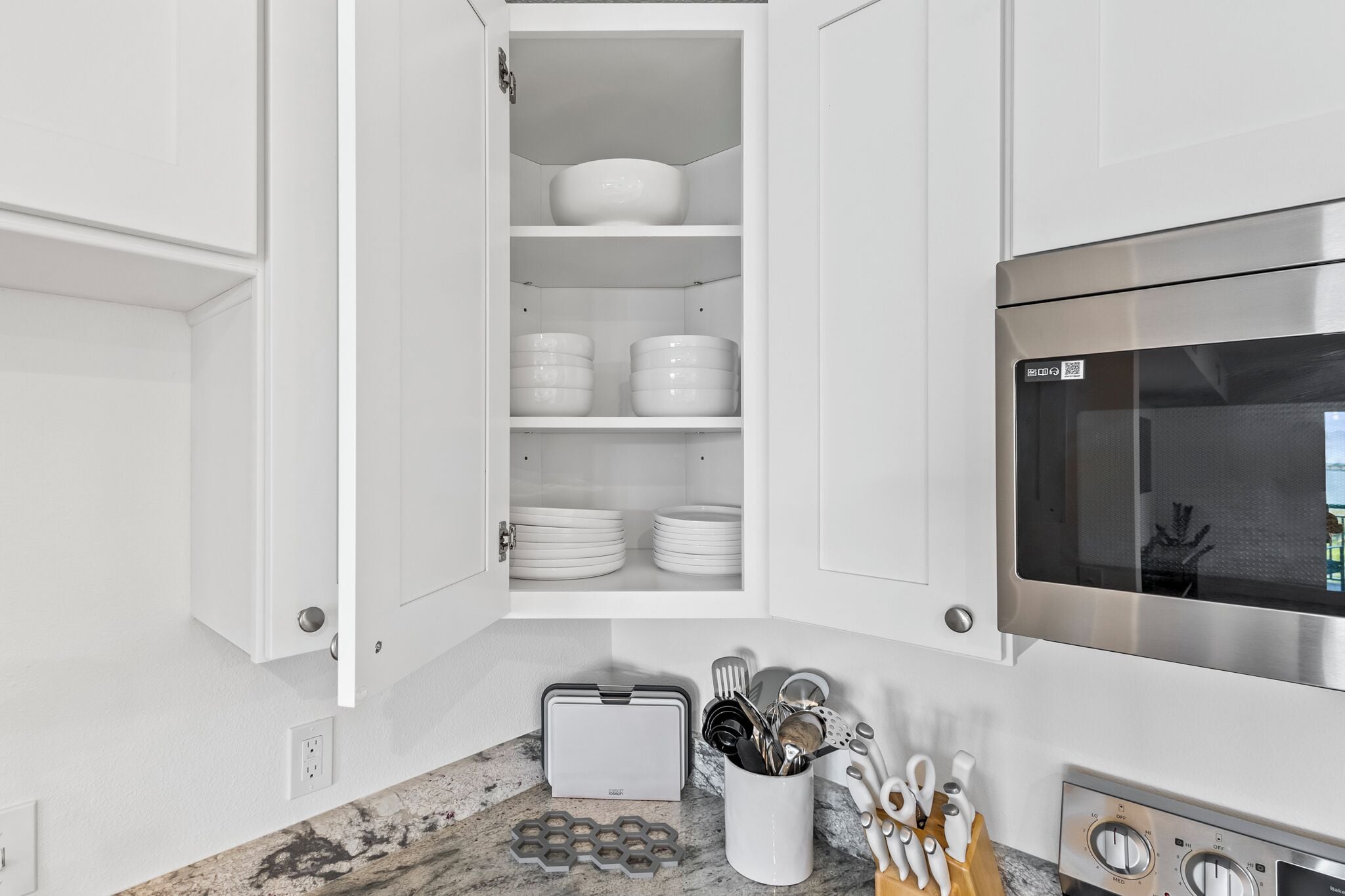 A kitchen with white cabinets, a microwave, and a countertop with utensils and a toaster.