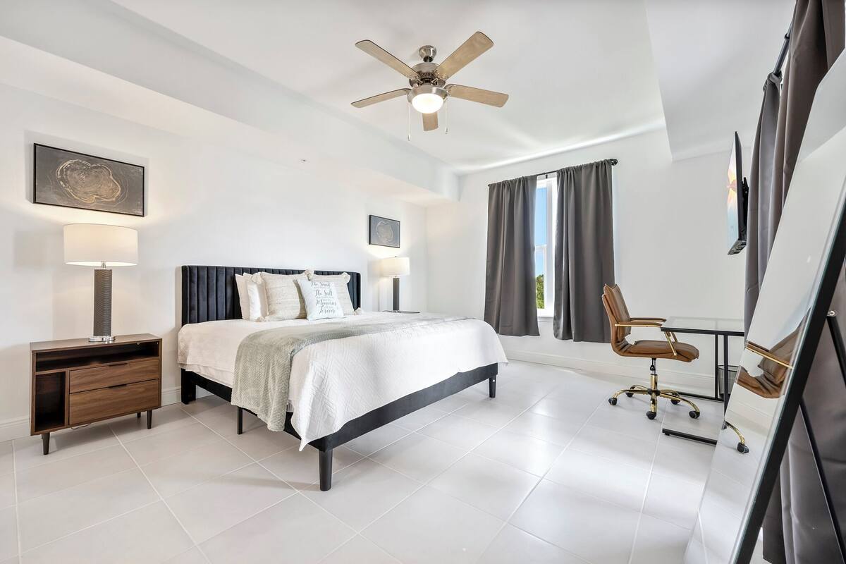 A modern bedroom with a bed, bedside tables, a desk, and a ceiling fan.