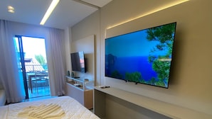 Een hotelkamer met een bed, een aan de muur bevestigde televisie en een balkon met uitzicht op zee.