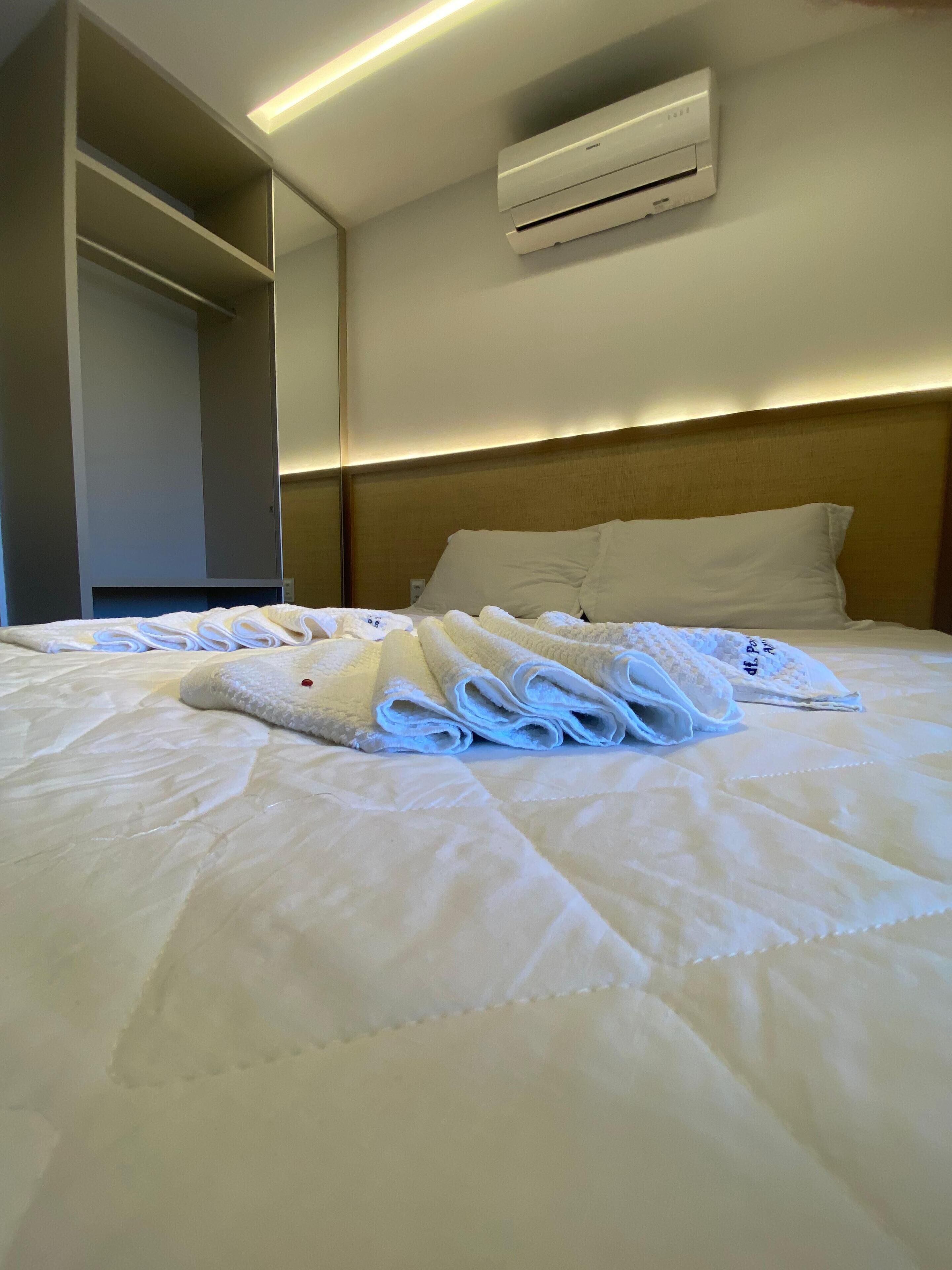 Una cama bien hecha con toallas dobladas, un cabecero y un equipo de aire acondicionado en la pared.