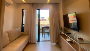 Een moderne hotelkamer met een bank, een televisie op een glazen plank en een schuifdeur naar een balkon.