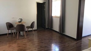 A room with a wooden floor, a small round table with chairs, a kettle, and a door leading to another room.