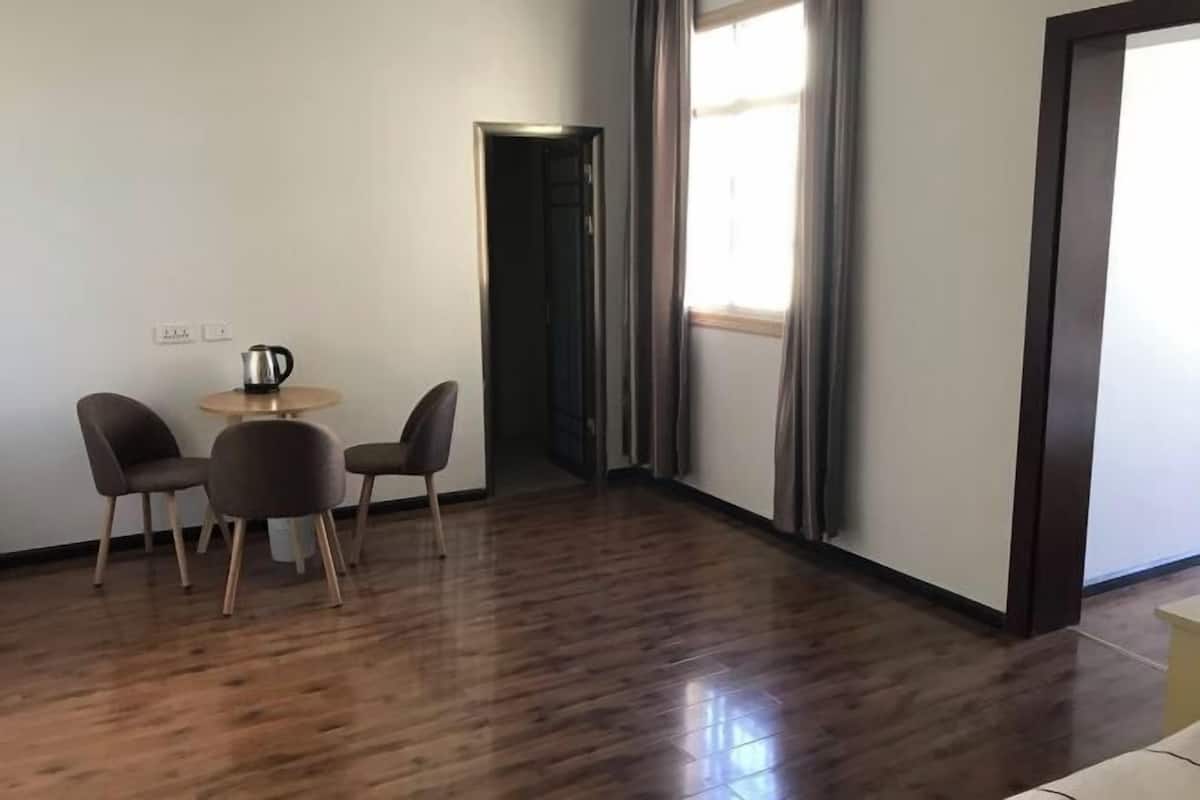A room with a wooden floor, a small round table with chairs, a kettle, and a door leading to another room.