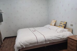 A single bed with a white mattress and two pillows, a wooden nightstand, and a wall-mounted TV. - Xiaocheng Zhijia Hotel (Chengjiang)