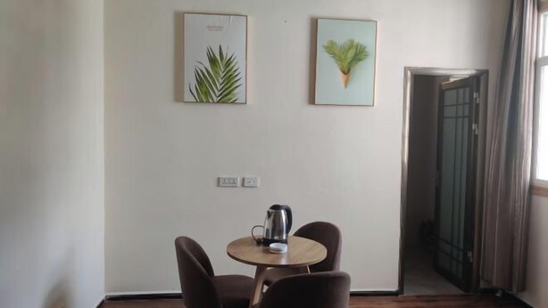 A room with a round table, two chairs, a kettle, and two framed botanical prints on the wall.