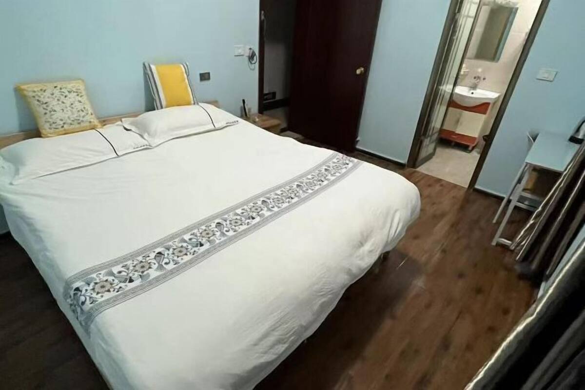 A bedroom with a bed, a bedside table, a mirror, and a bathroom visible through an open door.