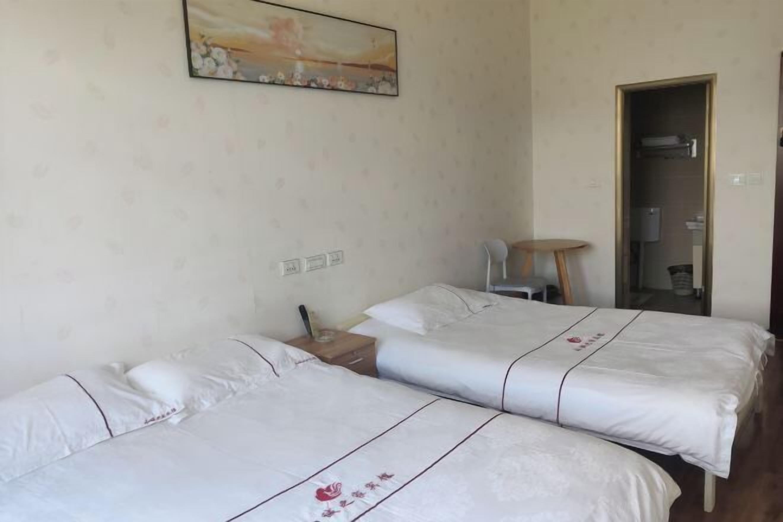 A hotel room with two beds, a small table, a chair, and a painting on the wall.
