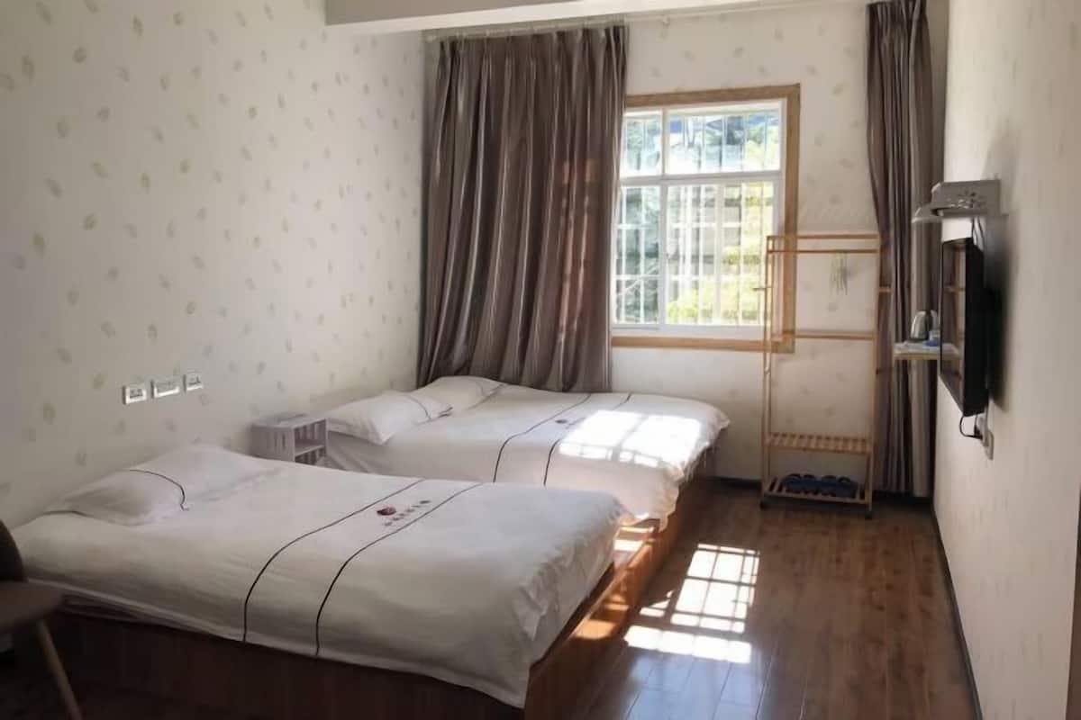 A room with two beds, a window with curtains, a TV, and a shoe rack.