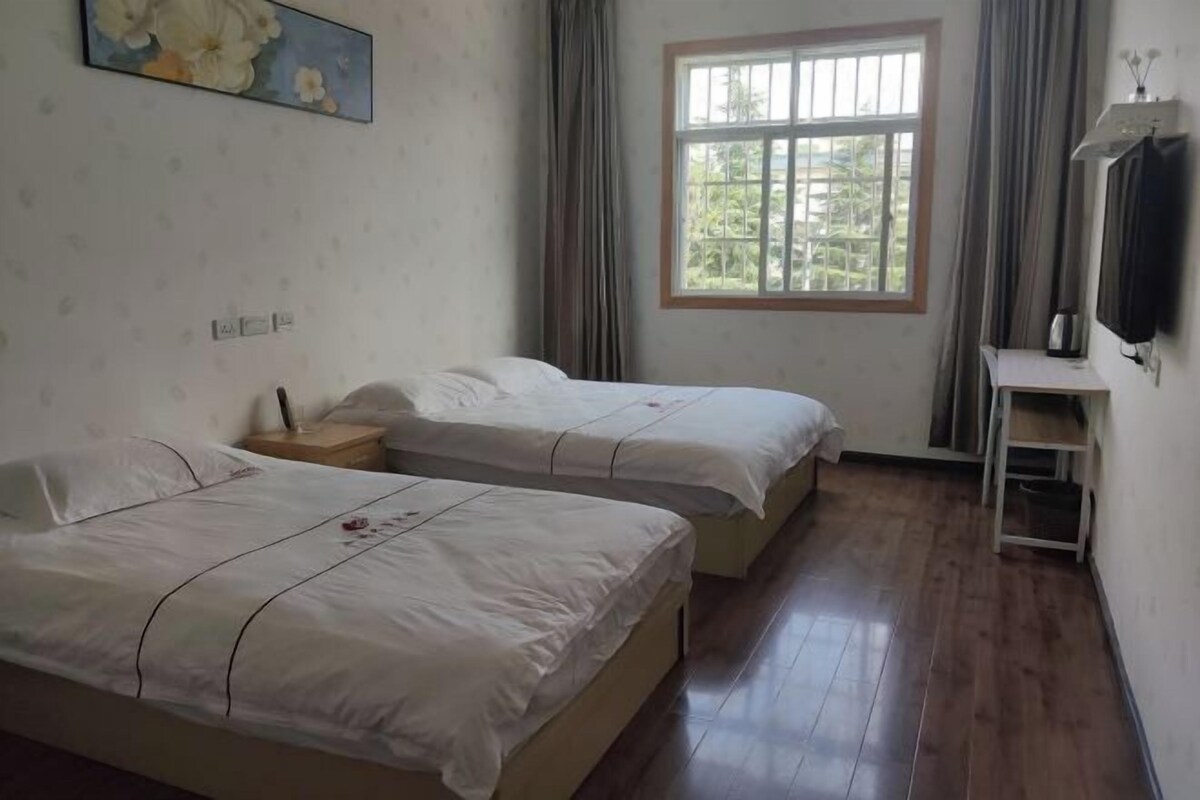 A hotel room with two beds, a window with curtains, a TV on a stand, and a painting on the wall.