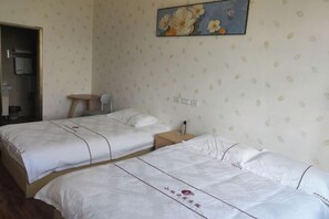 A hotel room with two beds, a small wooden table, and a painting on the wall. - Xiaocheng Zhijia Hotel (Chengjiang)