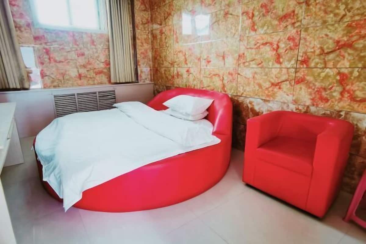A room with a bed, a red chair, and a window with curtains.