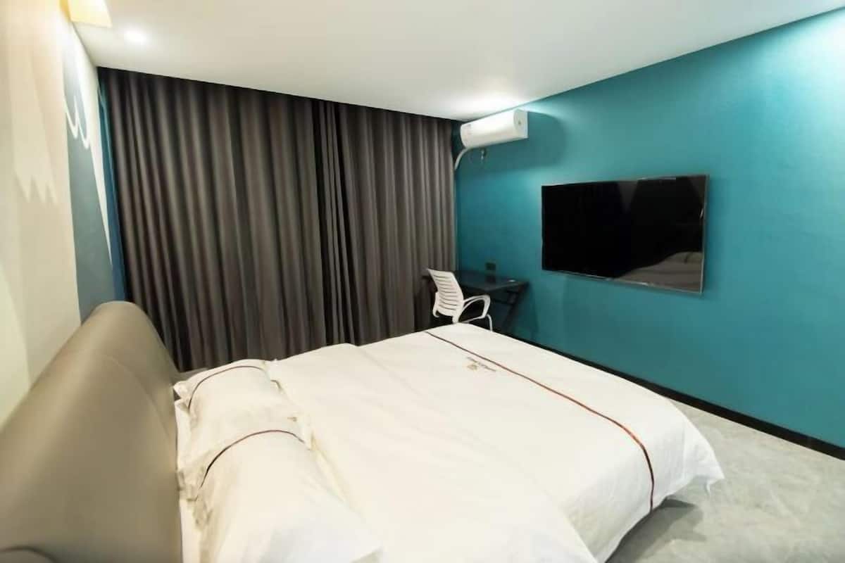 A hotel room with a bed, a desk, a chair, a TV, and a curtain.