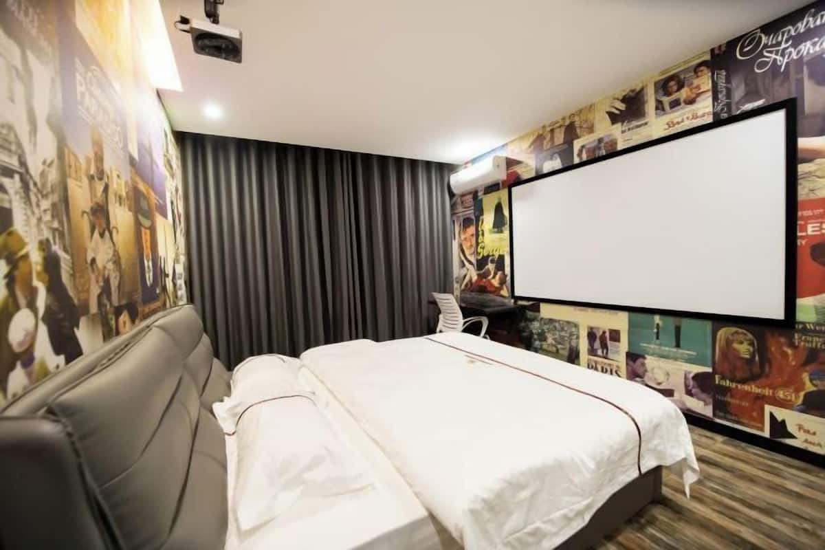 A hotel room with a bed, a desk, and a large poster on the wall.