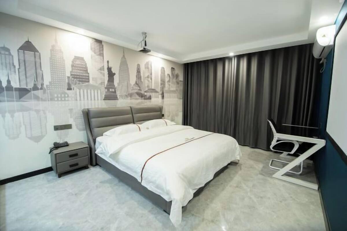 A modern hotel room with a cityscape mural, a bed, a bedside table, and a chair.