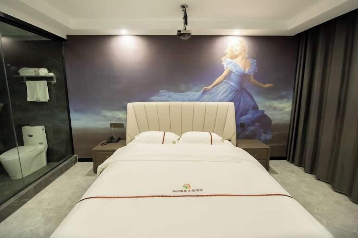 A hotel room with a large bed, a nightstand, a wall-mounted TV, a bathroom with a toilet and towel rack, and a large window with curtains.