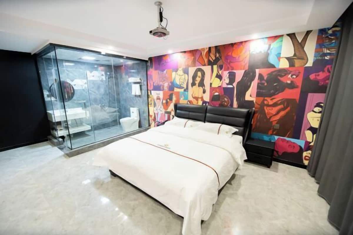 A bedroom with a bed, a glass partition, and a colorful mural on the wall.
