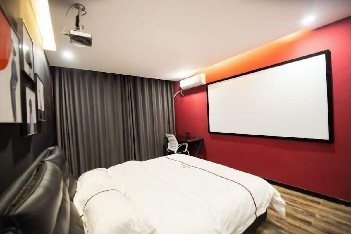 A hotel room with a bed, a desk, a chair, a projector, and a large blank screen on the wall.