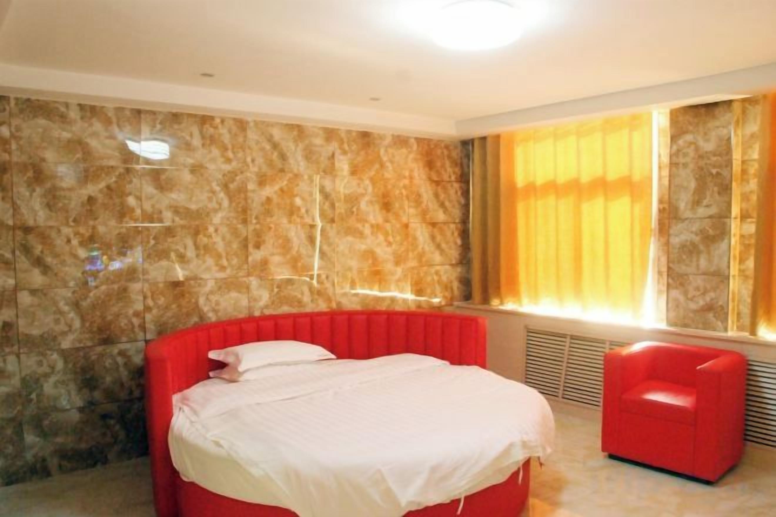 Une chambre avec un lit rouge, une chaise rouge et un mur en pierre.