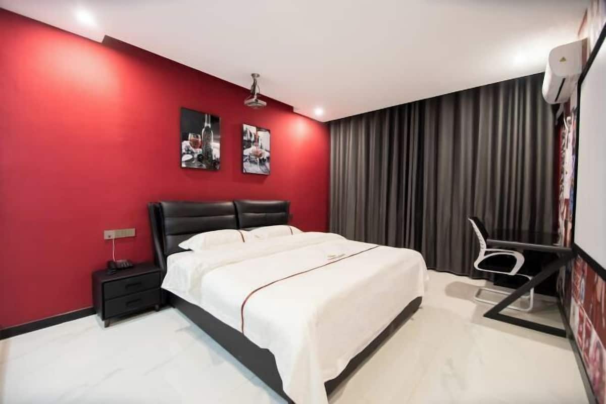 A modern bedroom with a black headboard, a white bedspread, a nightstand with a phone, a desk with a chair, and a large window with curtains.