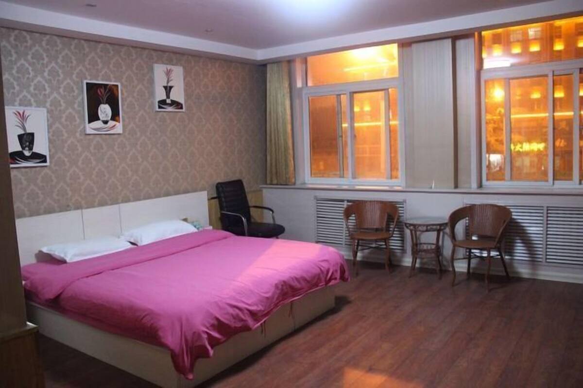 A bedroom with a bed, two chairs, a radiator, and a window with curtains.