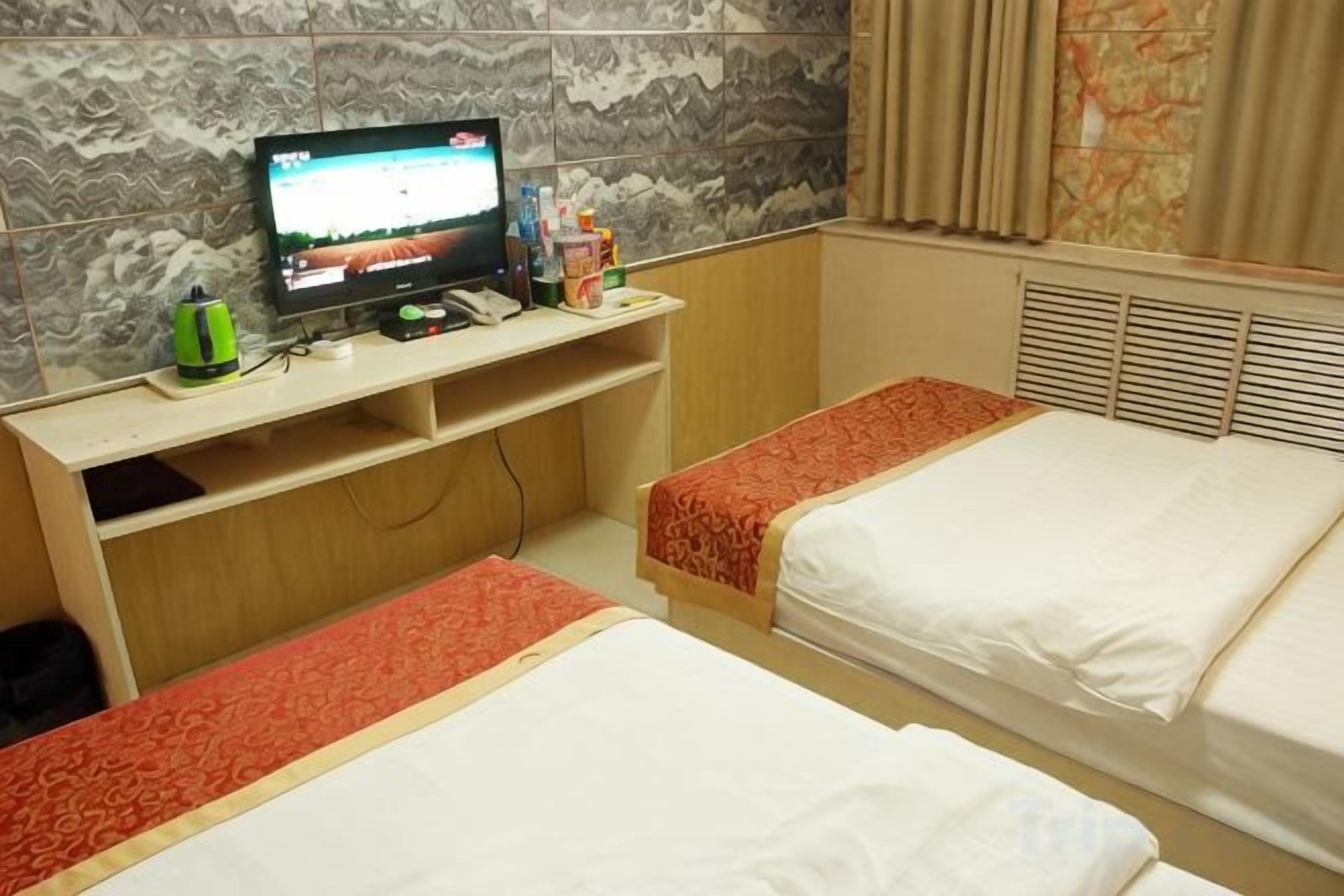 A hotel room with two beds, a TV on a wooden stand, and a window with curtains.