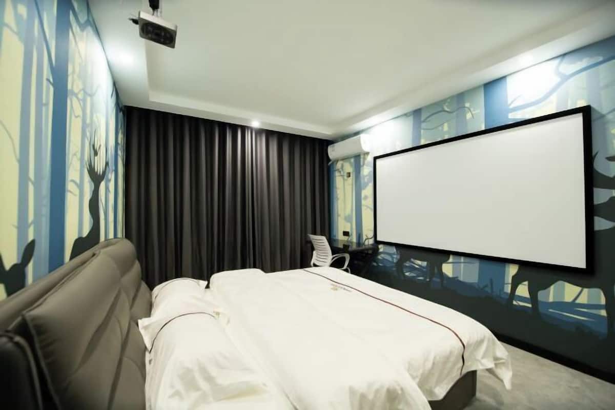 A hotel room with a bed, a projector screen, a couch, and a wall with a mural.