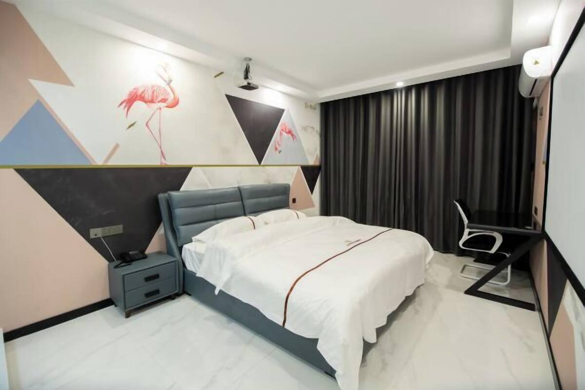 A modern hotel room with a bed, bedside table, and a desk with a chair.