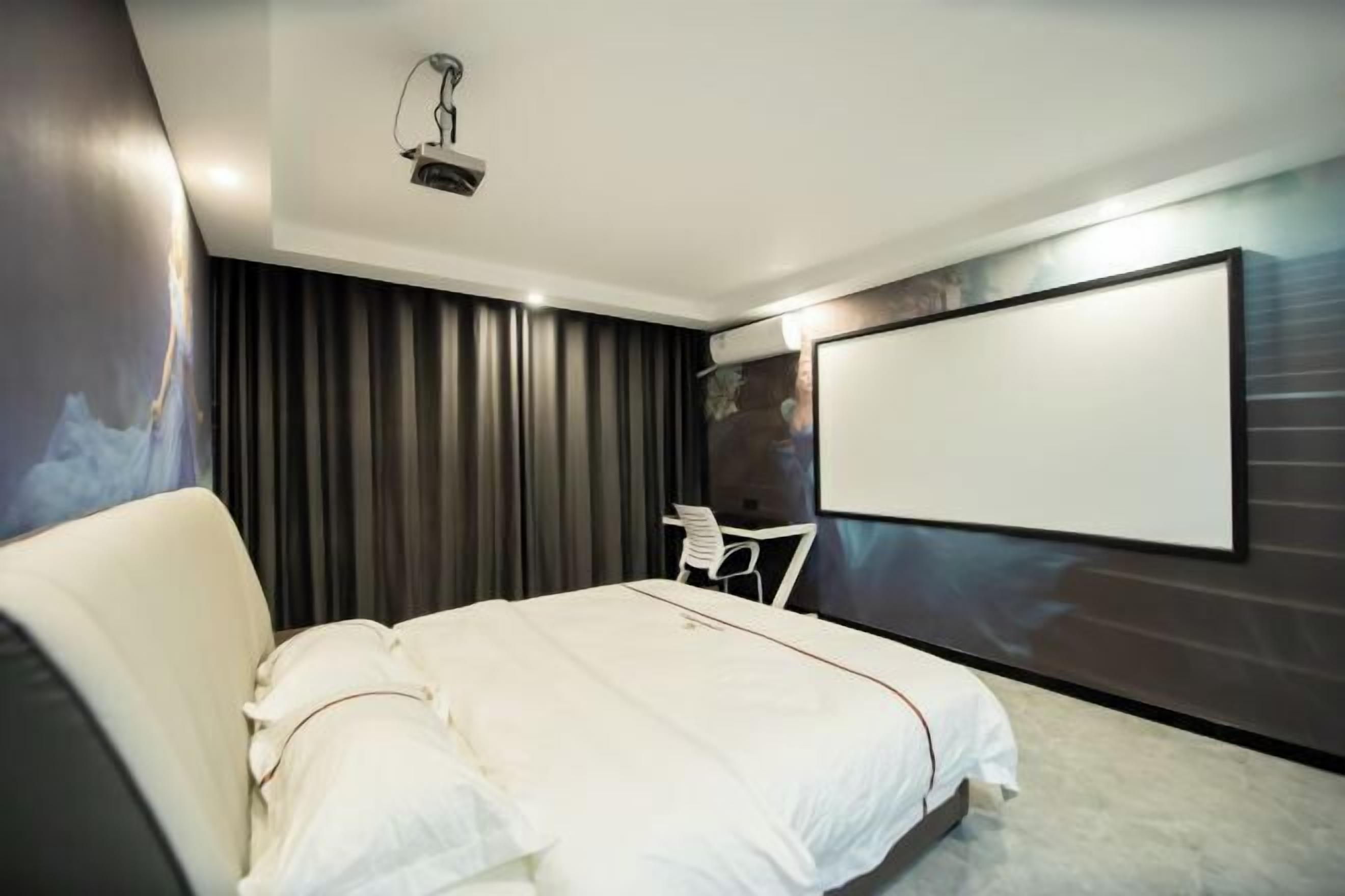 A modern hotel room with a large bed, a flat-screen TV mounted on the wall, and a ceiling projector.