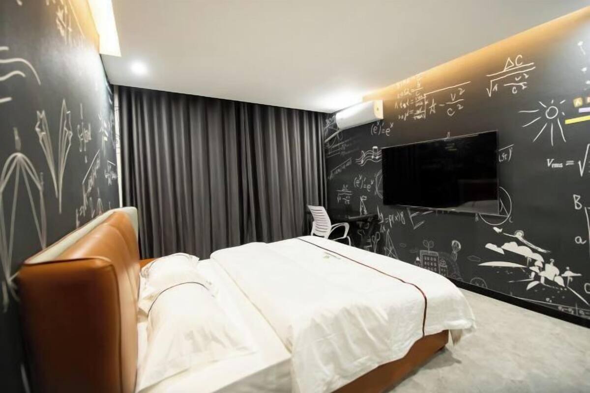 A modern bedroom with a bed, a TV, and a wall with mathematical equations.