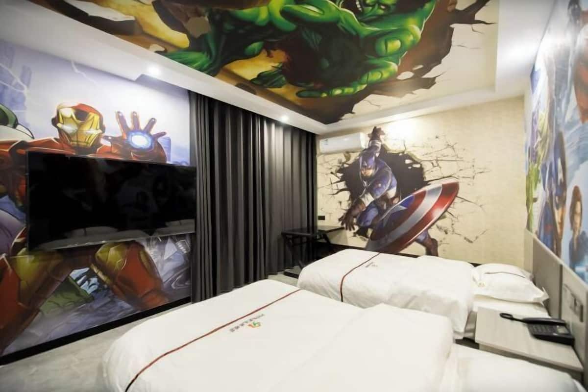 A hotel room with two beds, a TV, and a mural of Iron Man and Captain America on the wall.
