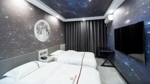 Hotelkamer met een bed, een bureau, een stoel, een televisie en een muur met een ontwerp van een sterrenhemel.