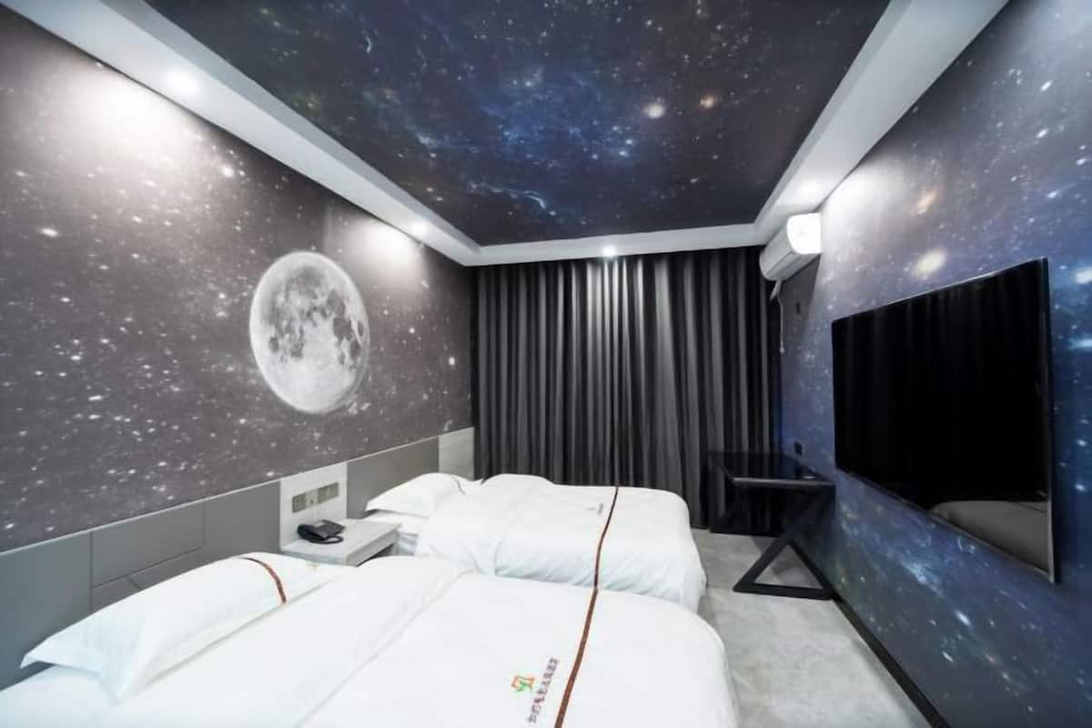A hotel room with a bed, a desk, a chair, a TV, and a wall with a starry sky design.