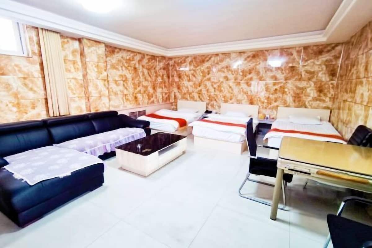 A hotel room with a black sofa, two single beds, a small table, and a chair.