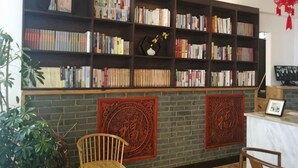 A bookshelf filled with books, two decorative wall hangings, and a chair.