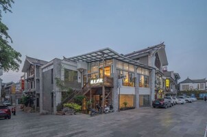 Un edificio tradicional con una entrada moderna, una escalera que conduce a la entrada y un aparcamiento con coches.