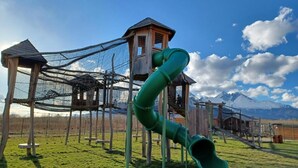 A playground with a green slide and climbing structures, set against a backdrop of mountains.
