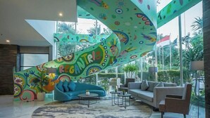 A modern living room with a colorful abstract wall, a blue sofa, a grey sofa, and a round coffee table. - Regantris Surabaya (Tegalsari)