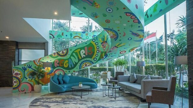 A modern living room with a colorful abstract wall, a blue sofa, a grey sofa, and a round coffee table. - Regantris Darmo Surabaya (Tegalsari)