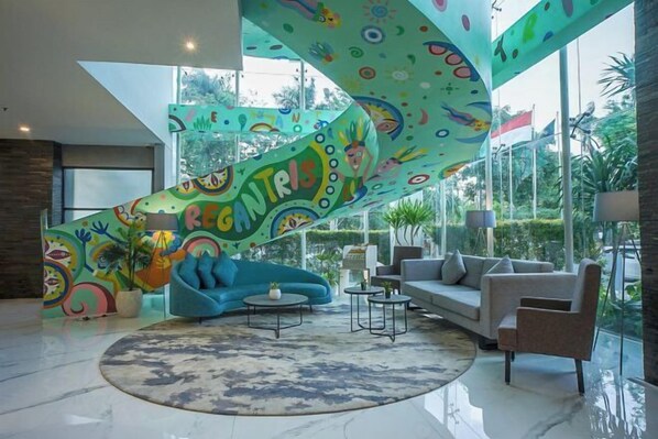 Un salon moderne avec un mur décoré d’une œuvre abstraite aux couleurs vives, un canapé bleu, un canapé gris et une table basse ronde.