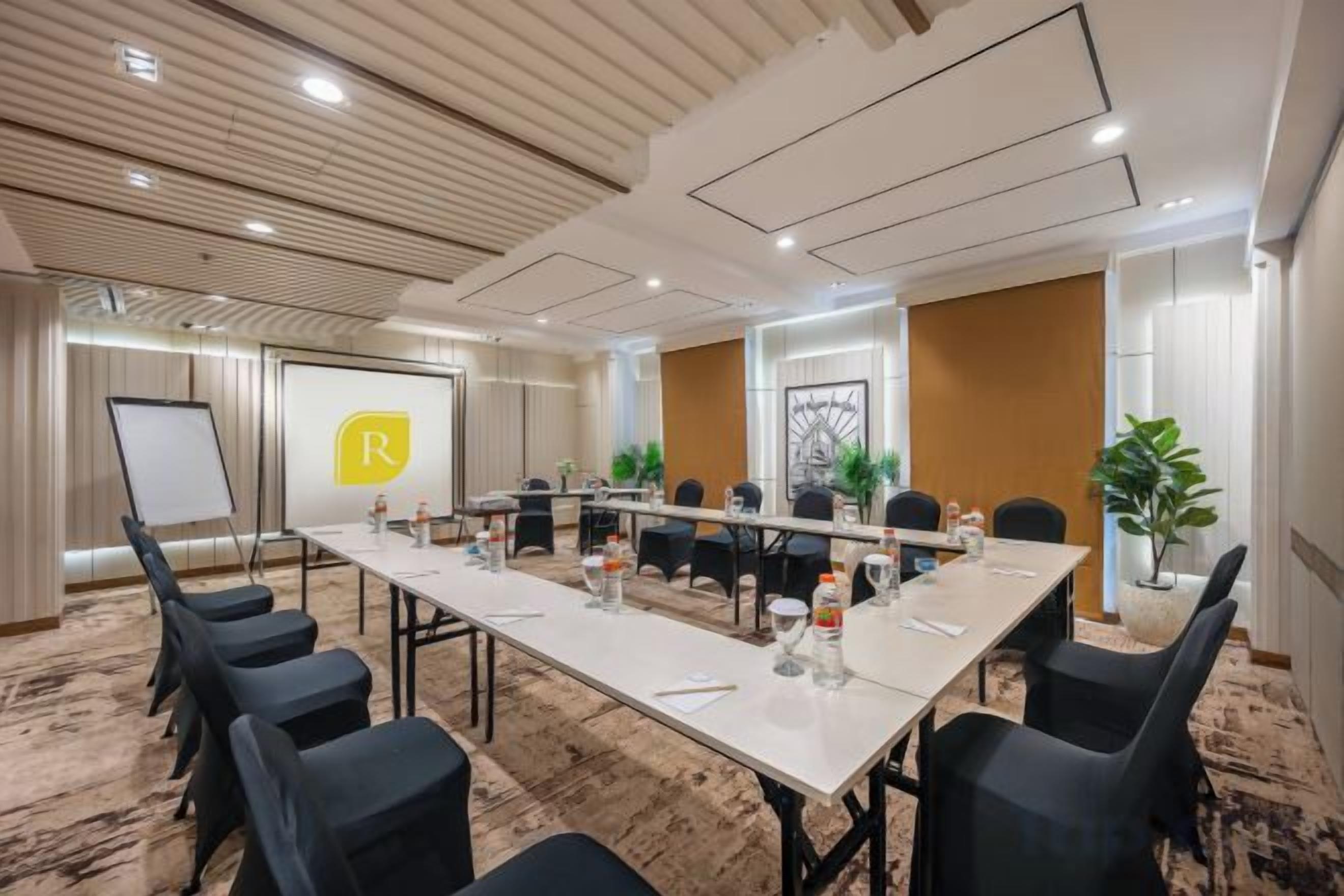 A conference room with a long table, chairs, a whiteboard, and a presentation screen.