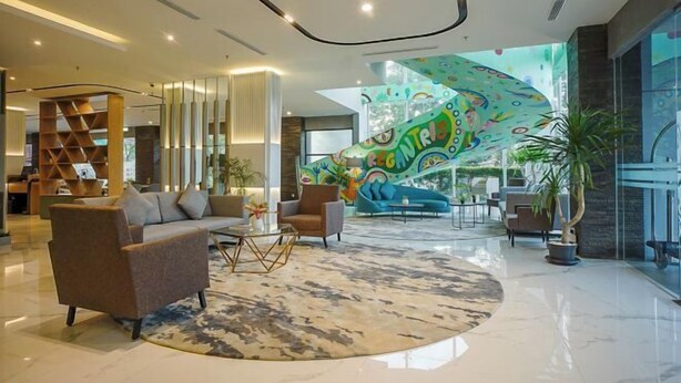 Un hall d’entrée spacieux au design moderne, comprenant un grand espace salon avec des canapés et des fauteuils, une table basse centrale et une fresque colorée sur le mur.