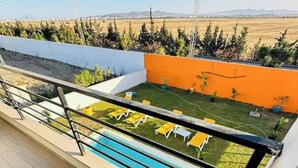 Un balcón con piscina, sillas reclinables amarillas y vistas a un campo y montañas.