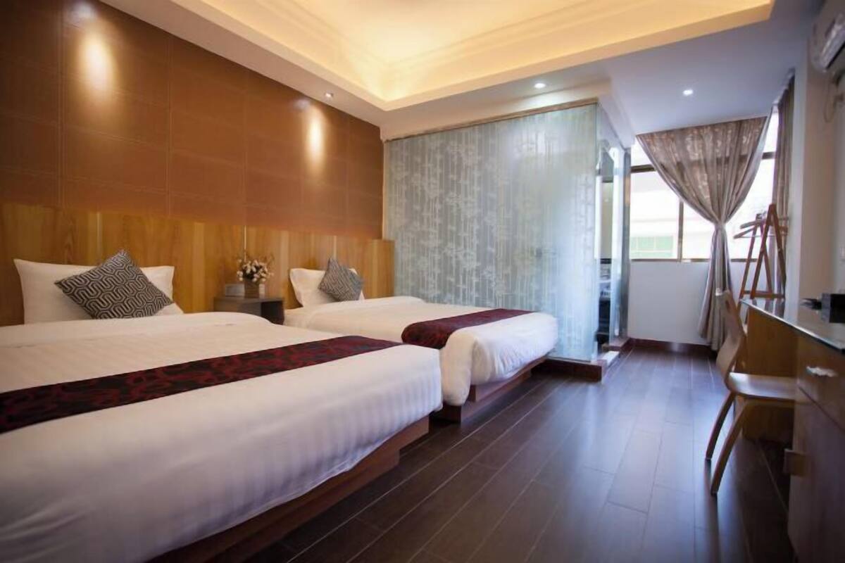 A hotel room with two beds, a desk, and a large window.