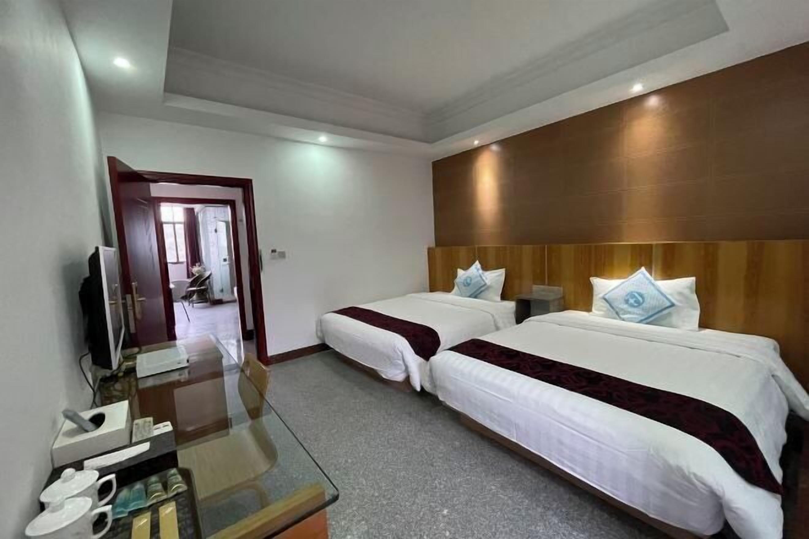 A hotel room with two beds, a TV, a glass table, and a door leading to another room.