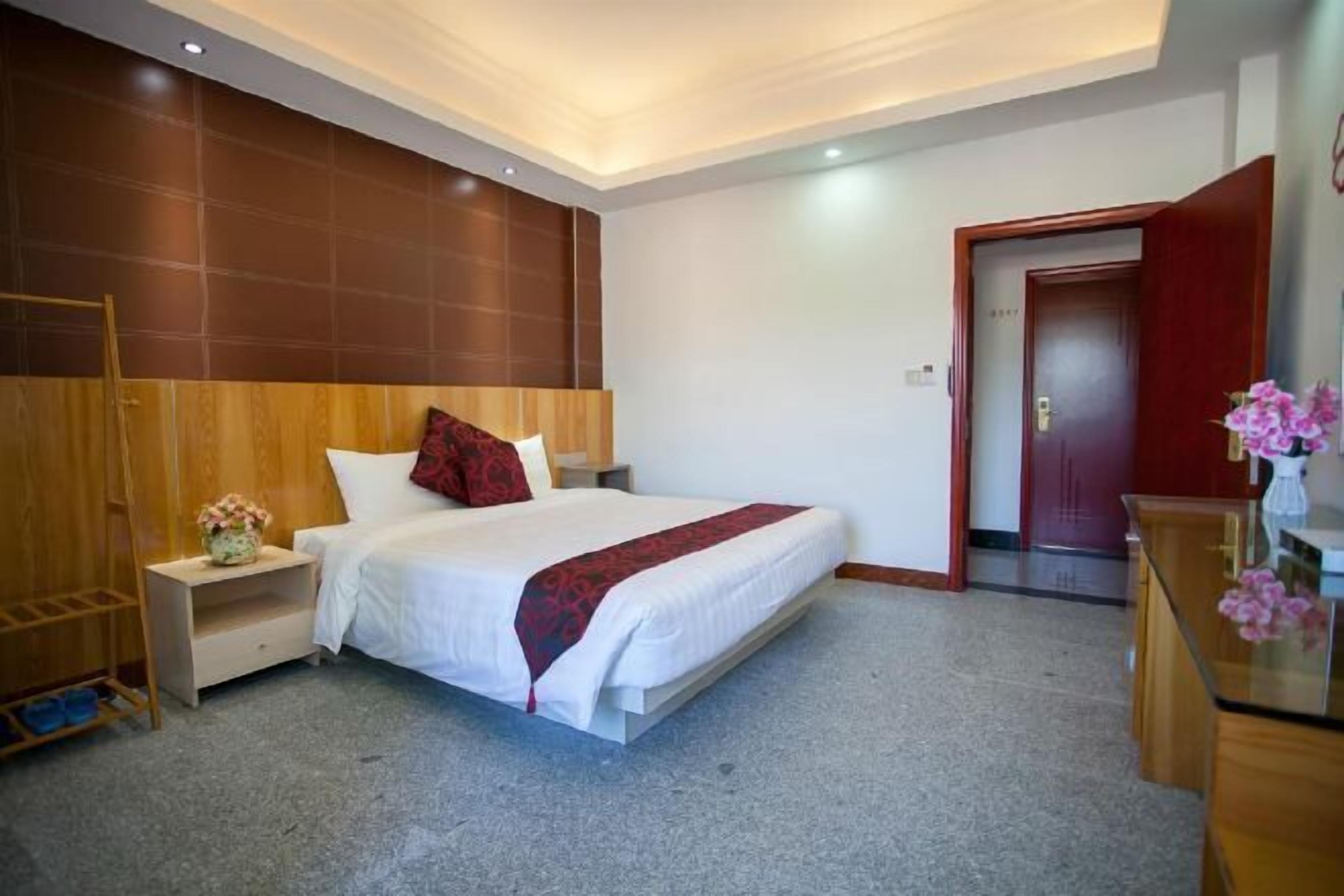 A hotel room with a bed, bedside table, nightstand, and a wooden wardrobe.
