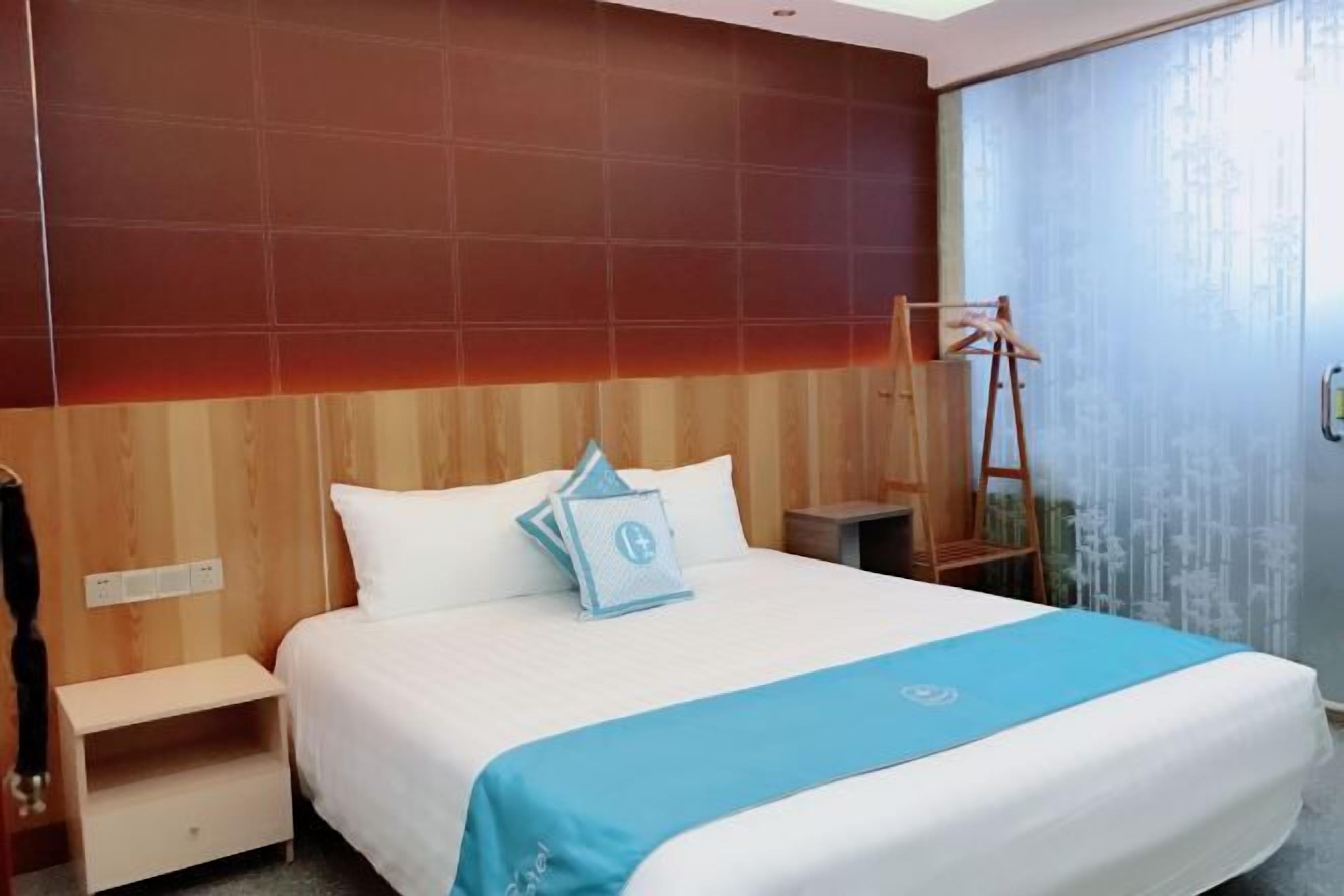 Una camera d'albergo con un letto, un comodino, una testiera in legno e una finestra con tende.