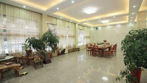 A spacious room with a polished floor, a dining area with wooden furniture, and several potted plants. - Starry Inn (Renhua)