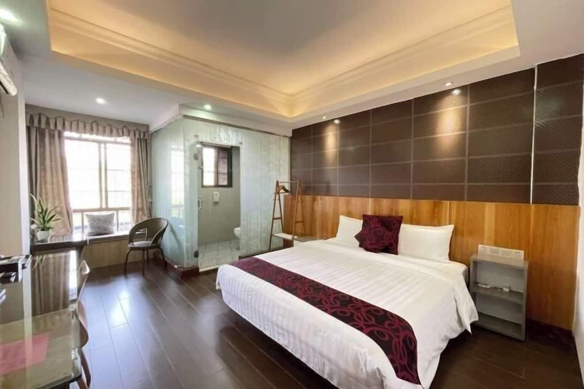 A hotel room with a large bed, a desk, a chair, a shower area, and a view of the outdoors.